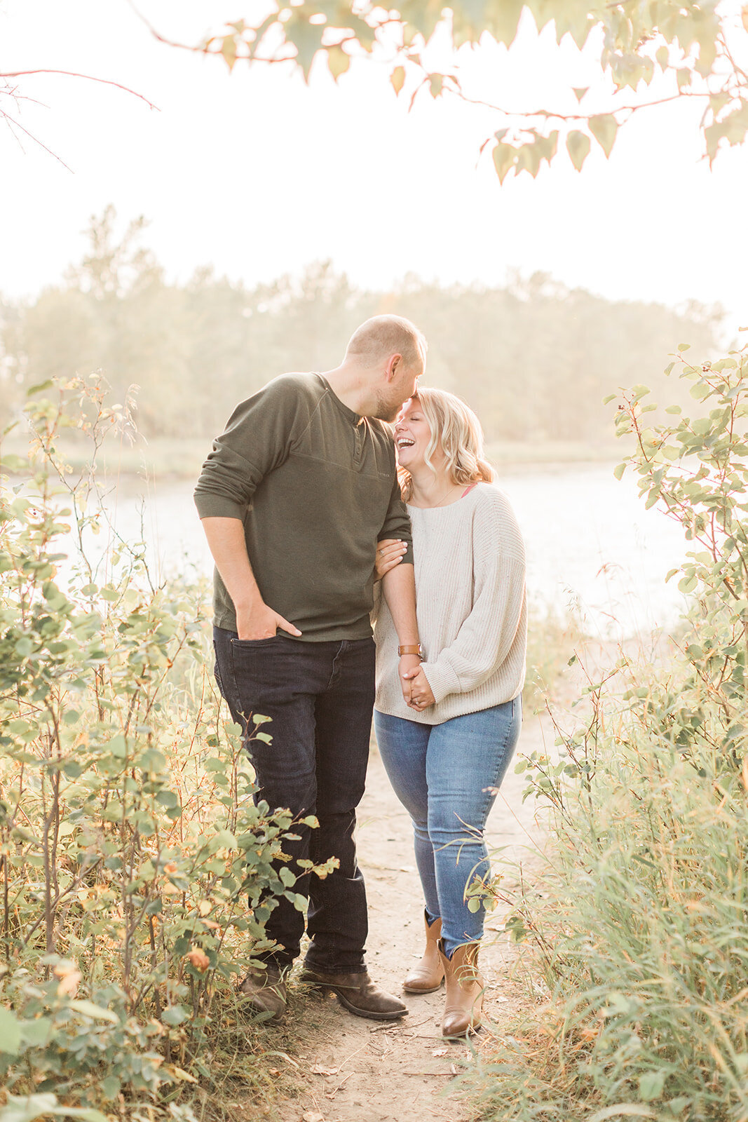 light and airy engagement photo of a man kissing womans forehead in front of the Bow River