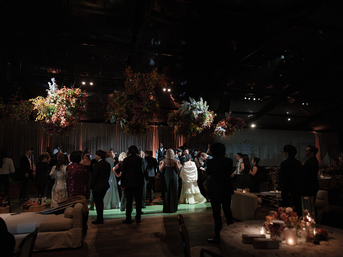 Interacting and sculptural floral clouds hang over the dance floor and bars of this fall wedding reception in Tennessee. Clear top tent build out for fall wedding reception in Tennessee hills.  Product clustered floral clouds in a tasteful fall color palette of copper, ruby, gold, burgundy, rust, and lavender. Orchids, bittersweet berries, butterfly ranunculus, and tulips are highlighted. Unique floral design with flower forward large scale installations. Design by Rosemary & Finch Floral Design in Nashville, TN.