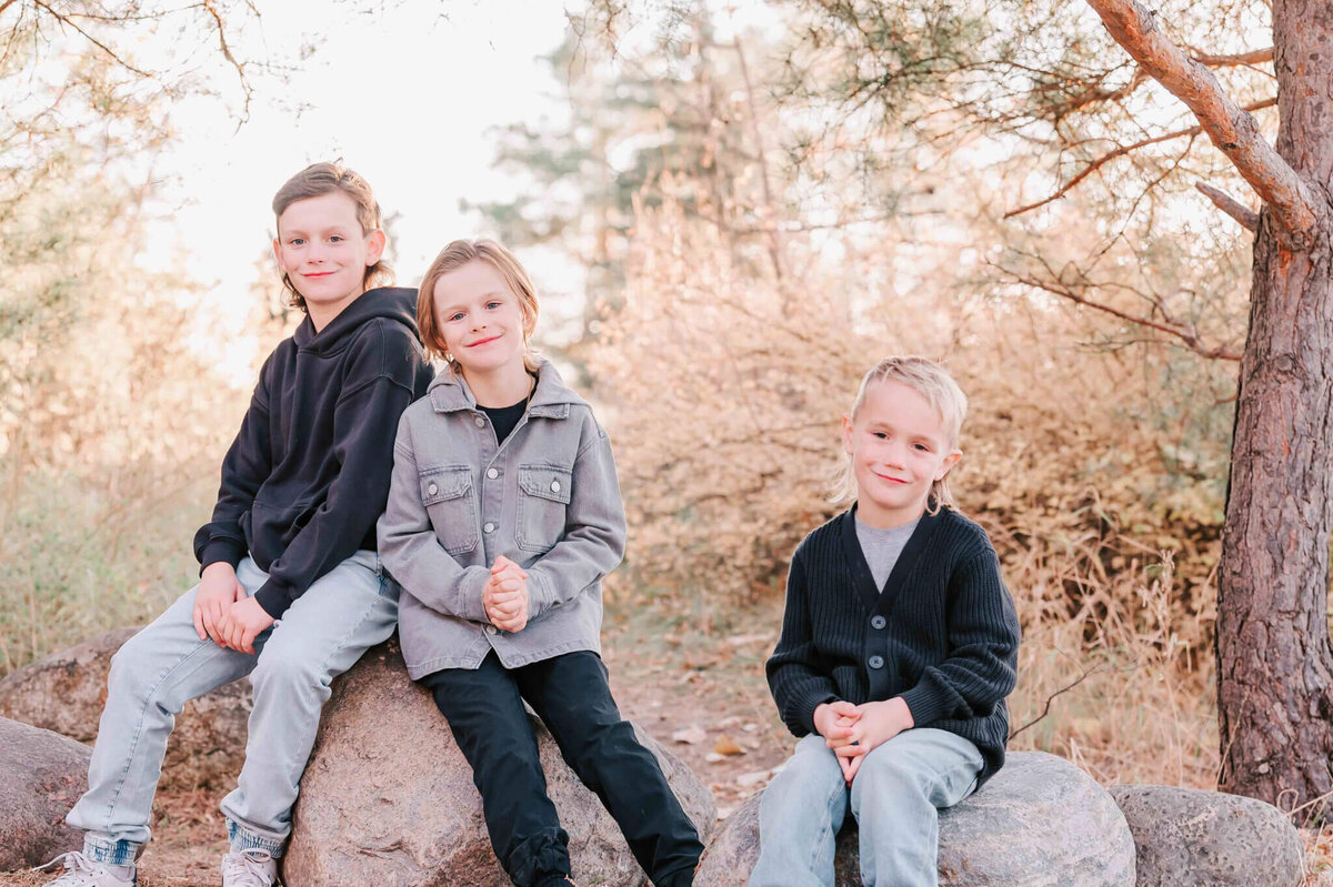 The 3 boys sit on the rocks by themselves. 