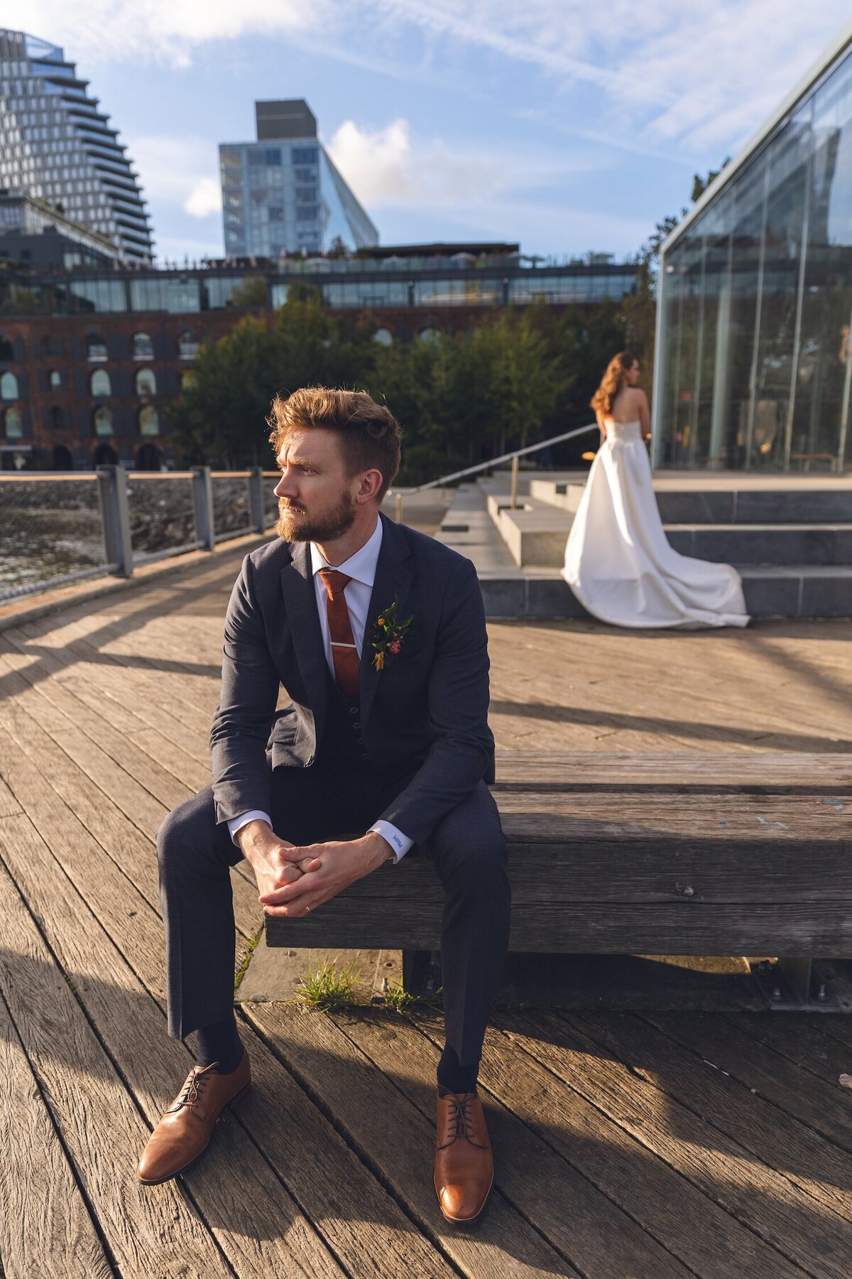 Groom sitting on bench with bride blurred in the background