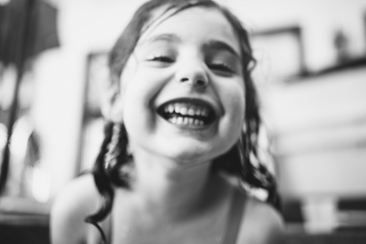 Blurry black & white image of young girl joyfully smiling towards camera taken by Los Angeles Family photographer Marjorie Cohen.