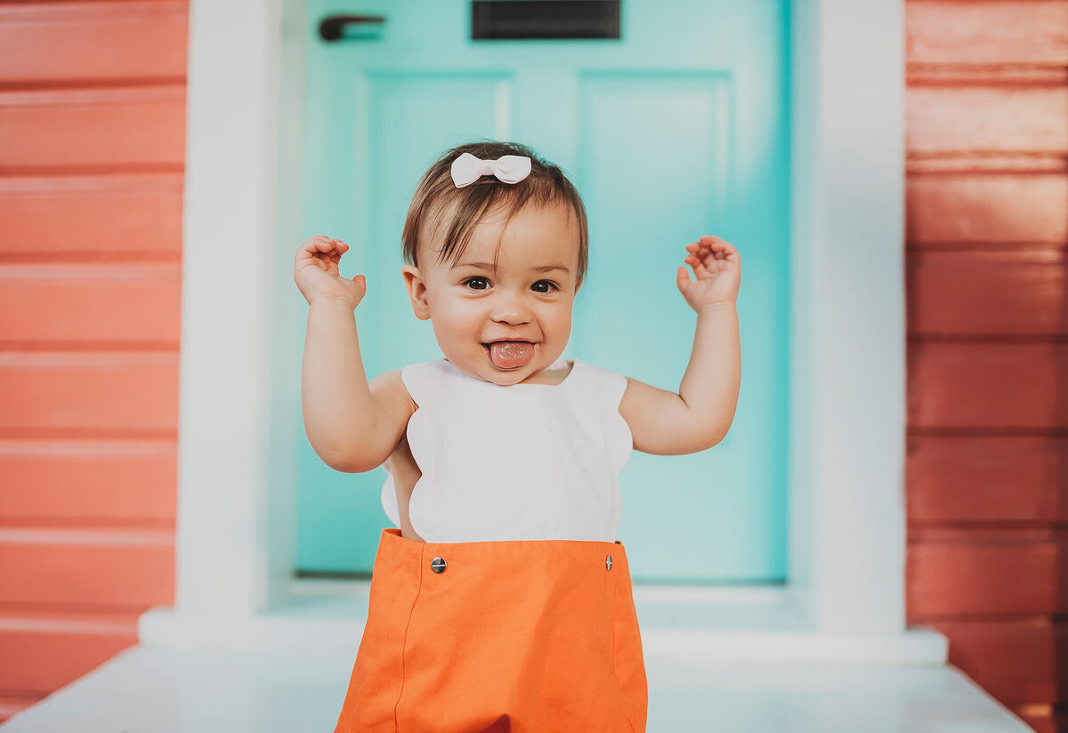 smiling baby girl in front of teal door and orange house in Fells Point Baltimore Maryland