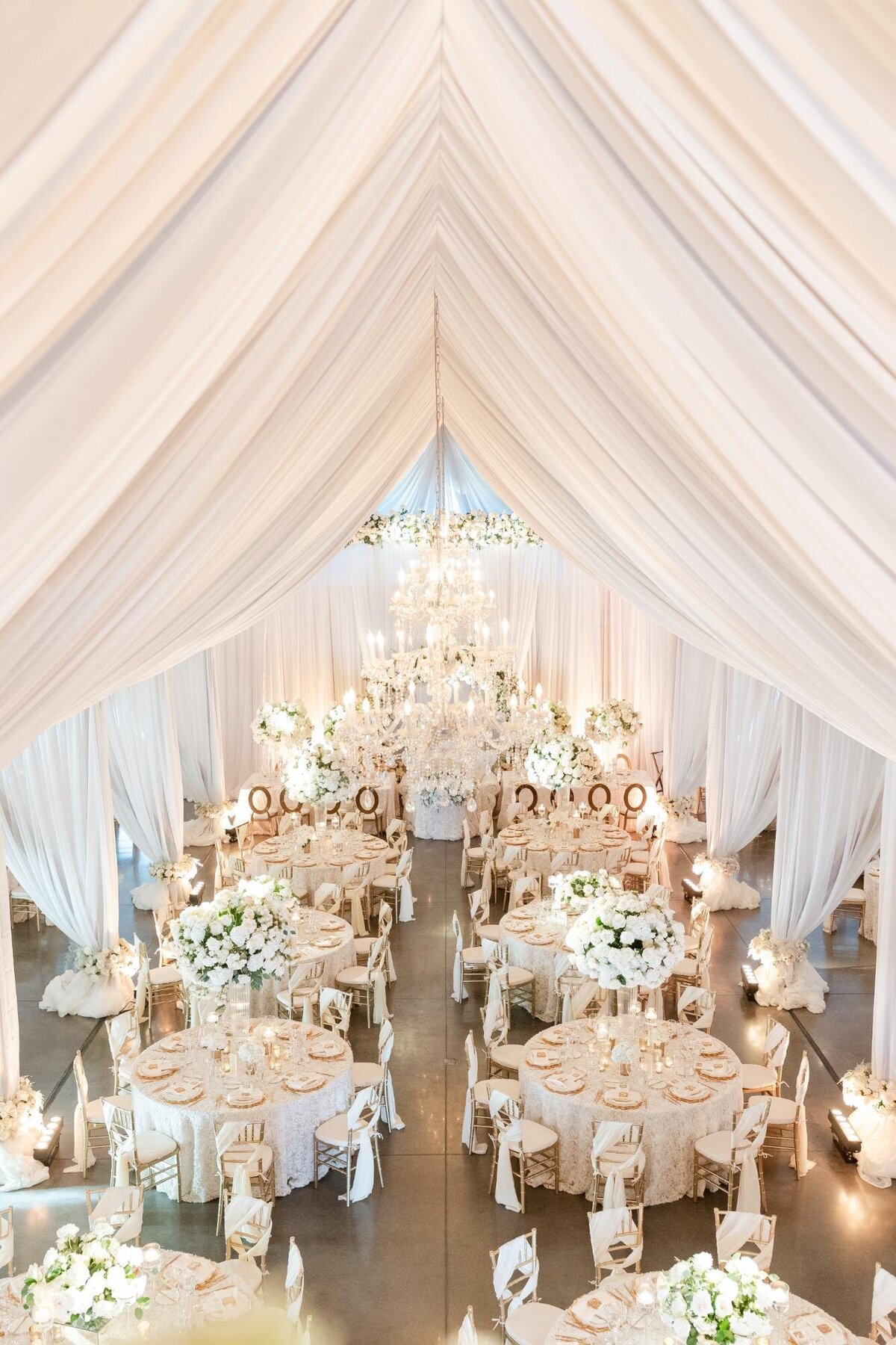 Elegant wedding reception hall with white drapery and floral centerpieces.