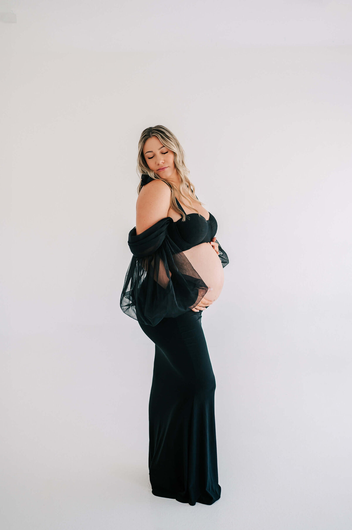 pregnant mom in black dress holding baby bump captured by Branson MO maternity photogarpher Jessica Kennedy of The XO Photography