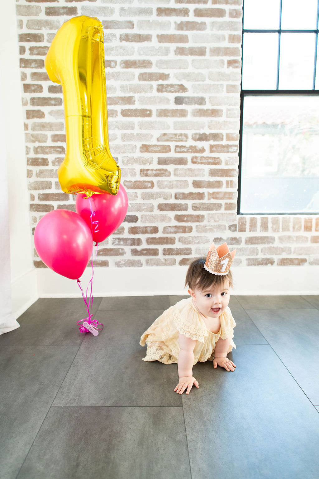 A small child crawling with a "1" crown on and balloons in the background.
