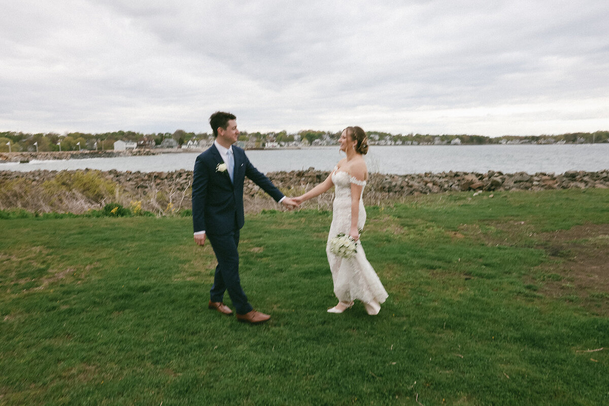 Bride and groom hold hands along the shore in Nahant, MA.