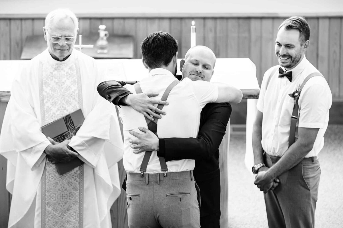 Groom hugging groomsman at church altar, Big Sky Chapel