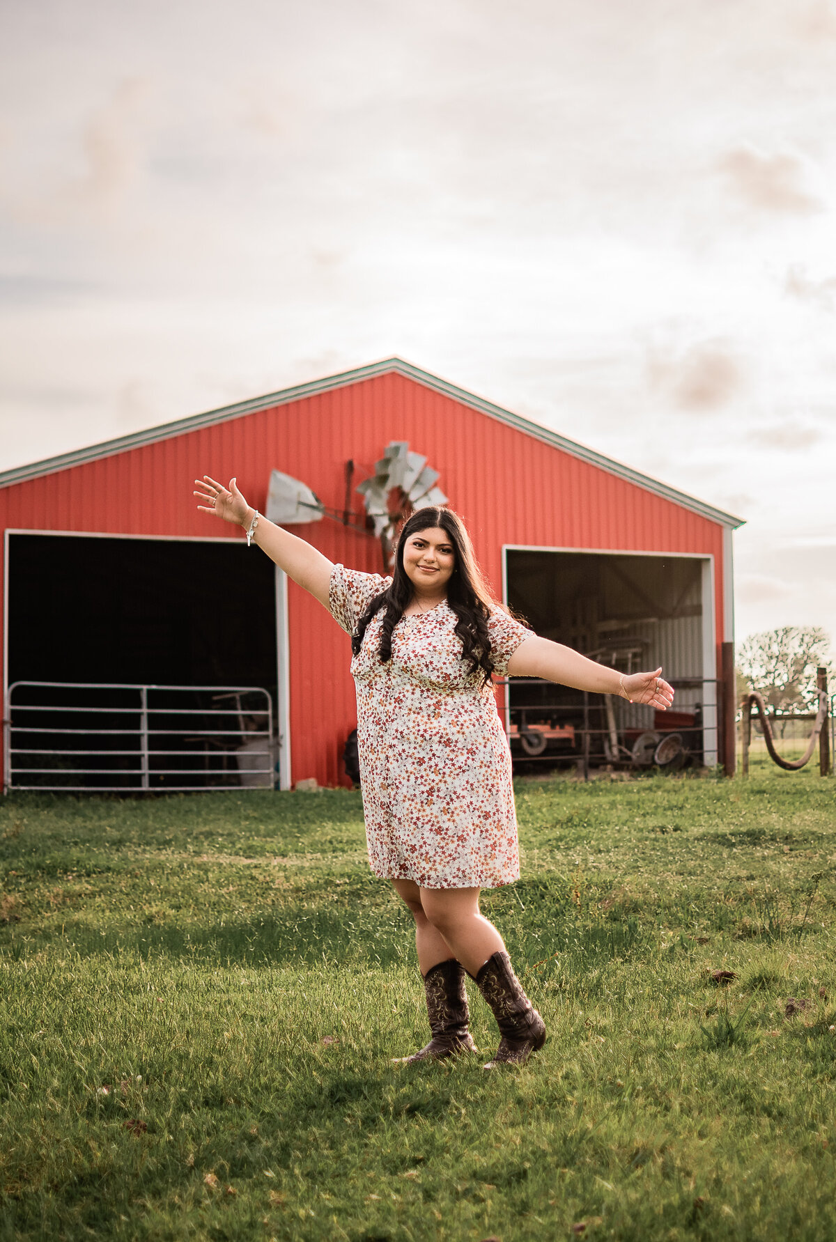 A Houston senior stands in front of a barn with her arms outstretched in Santa Fe, TX.