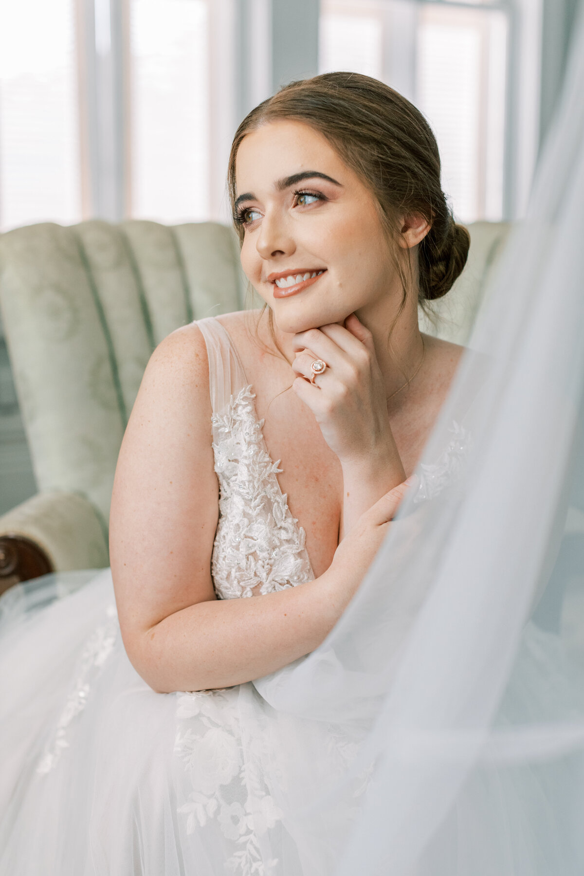 A bride sits on a vintage sofa while smiling off into the distance.
