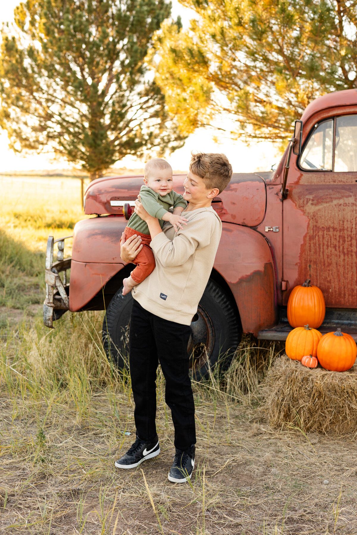 Preteen boy holds baby brother and smiles at him as baby brother smiles off-camera.