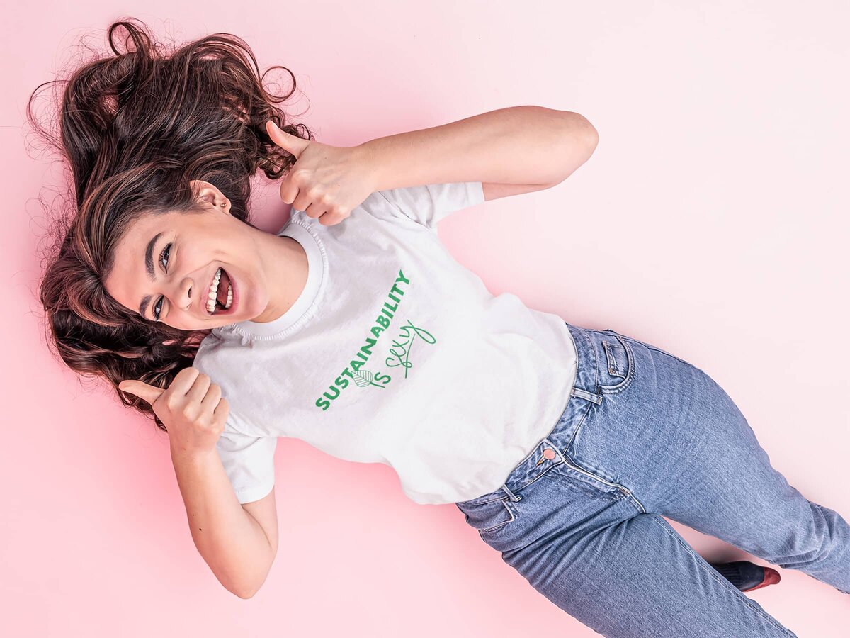 A happy, female model gives 2 thumbs up while wearing a white Sustainability is sexy tee
