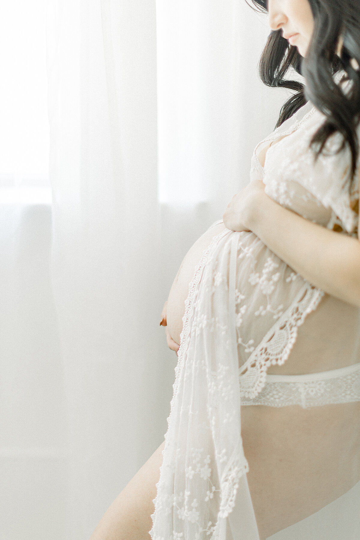 A close up side profile of an expecting mother standing by a window as being photographed by a Dallas maternity photographer in their studio.