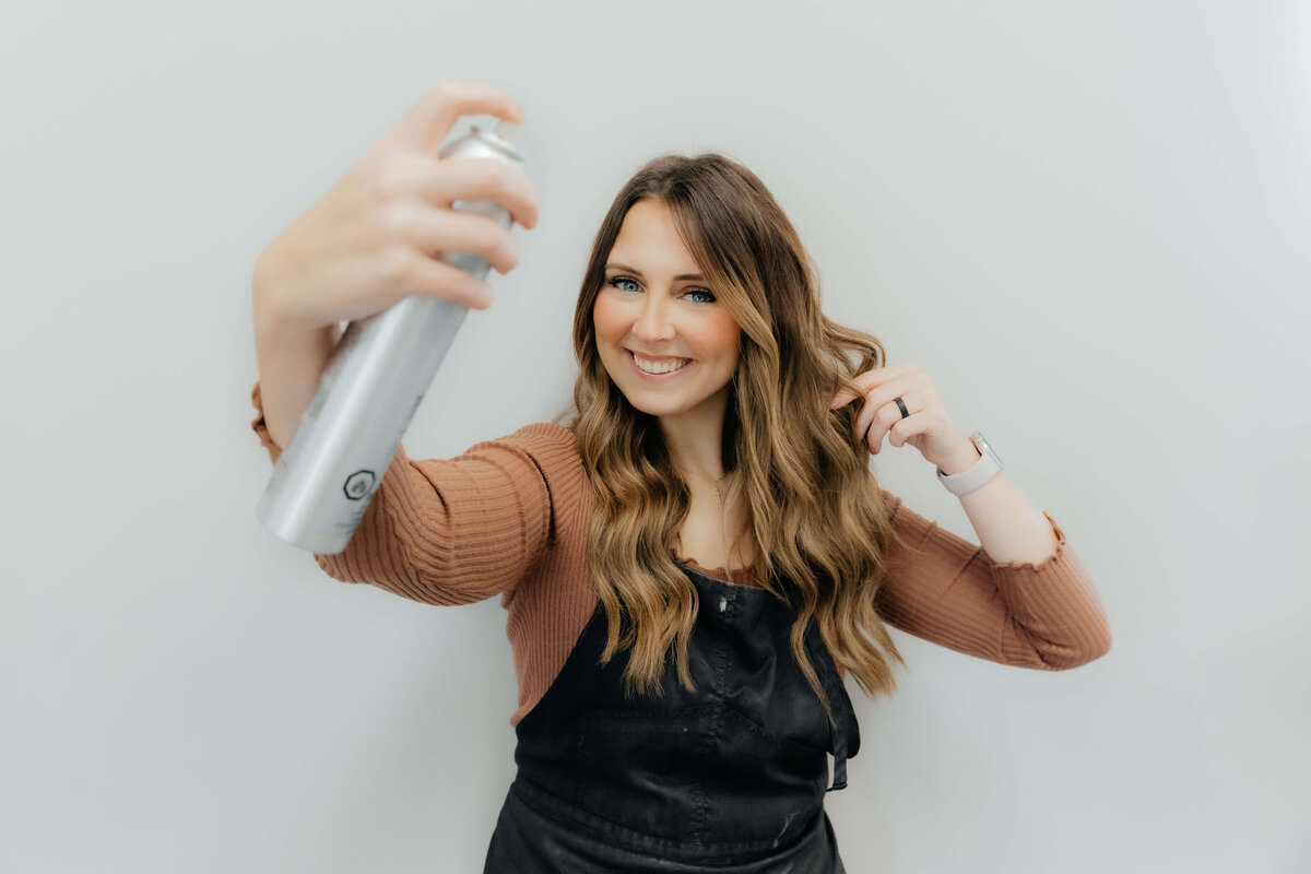 Smiling hairstylist using hairspray during brand shoot, Ohio brand photography for beauty professionals ready to elevate their visual identity