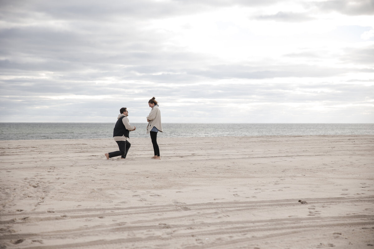Young man getting down on his knees as he about to propose at the empty Hamptons Beach.