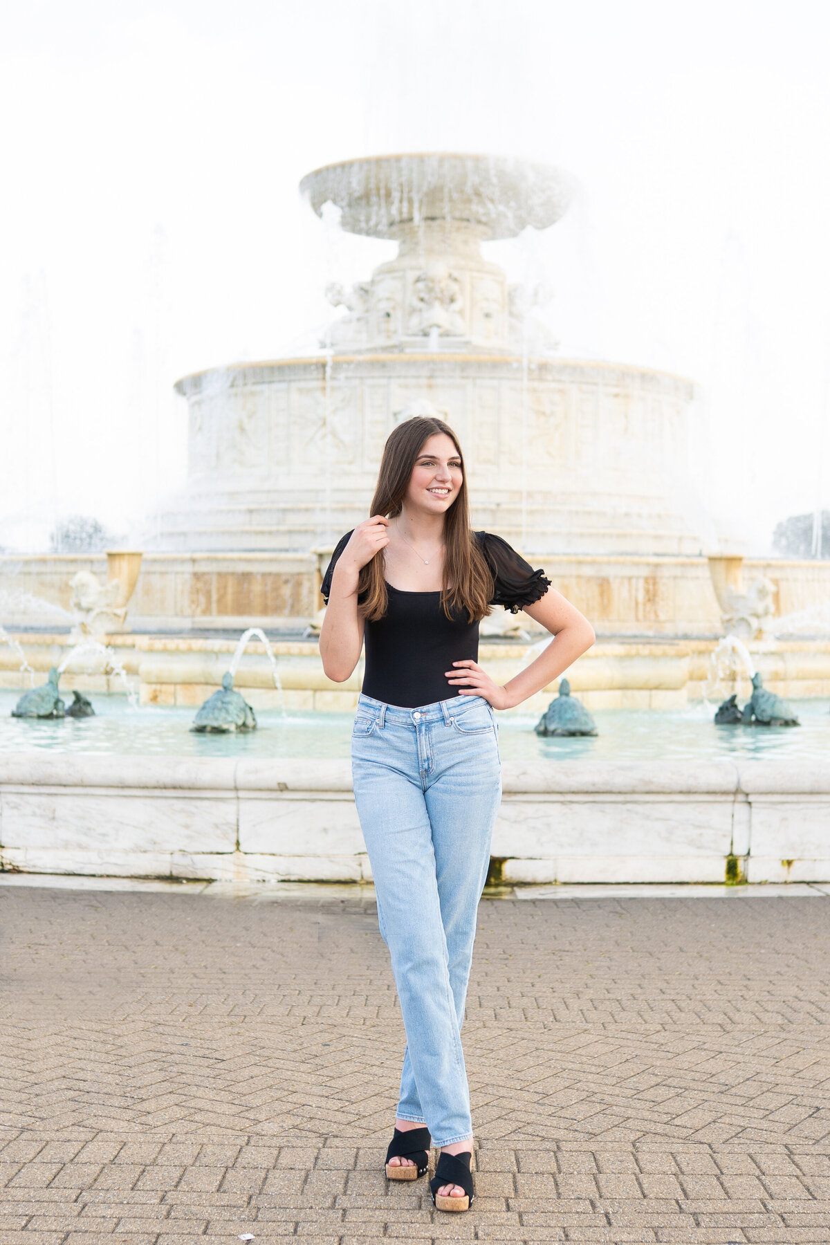 teenage girl standing with legs crossed playing with hair with James Scott Memorial Fountain behind her