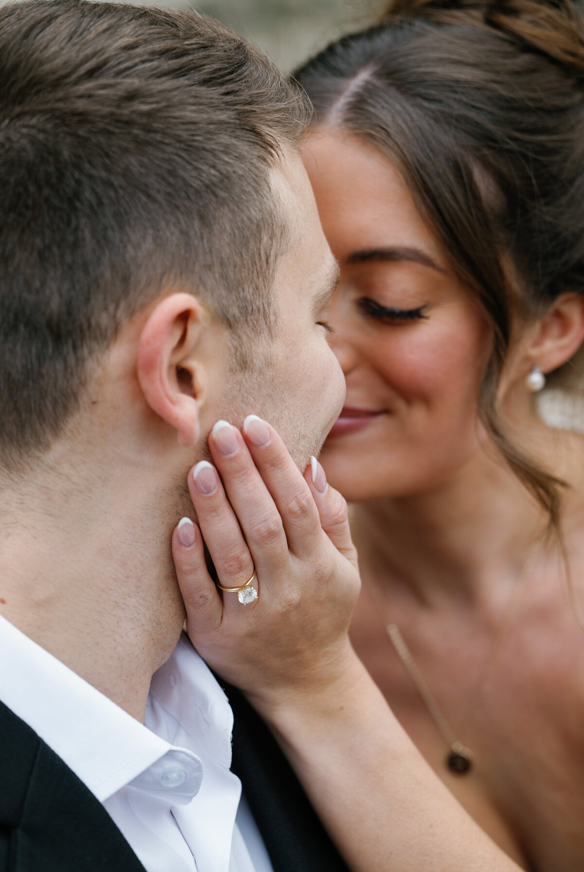 a bride hold her grooms face with her engagement ring showing