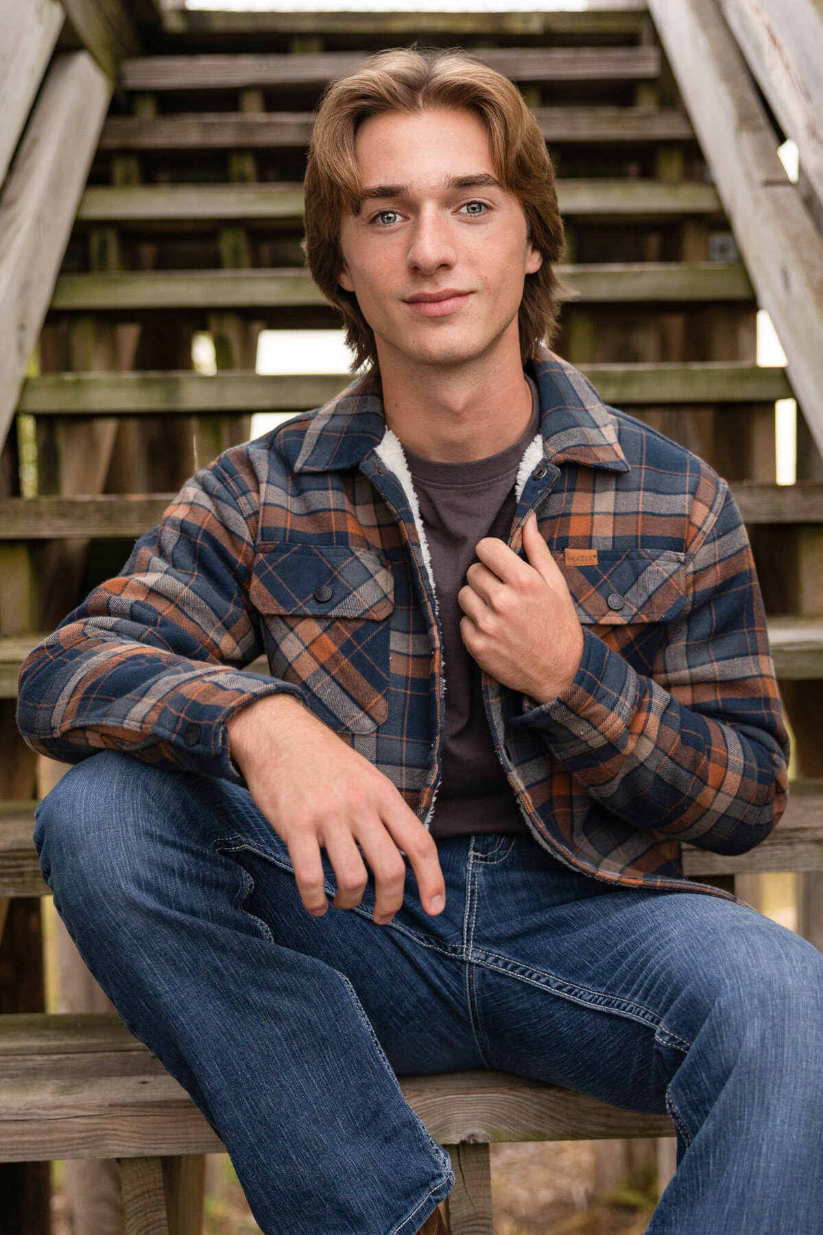 A senior guy sitting on wooden stairs holding his jacket in Lawrence, KS