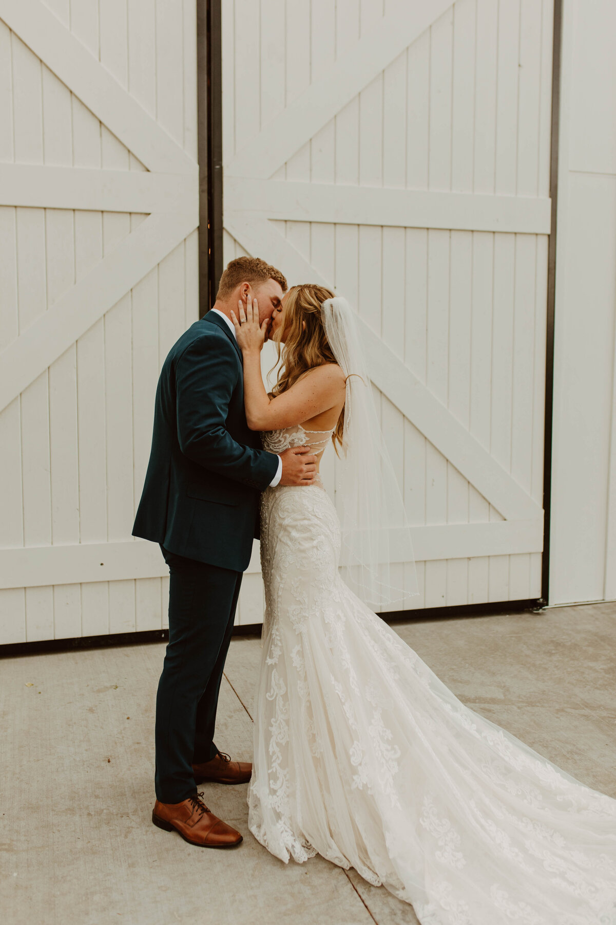 Bride and groom kissing in front of white barn doors.