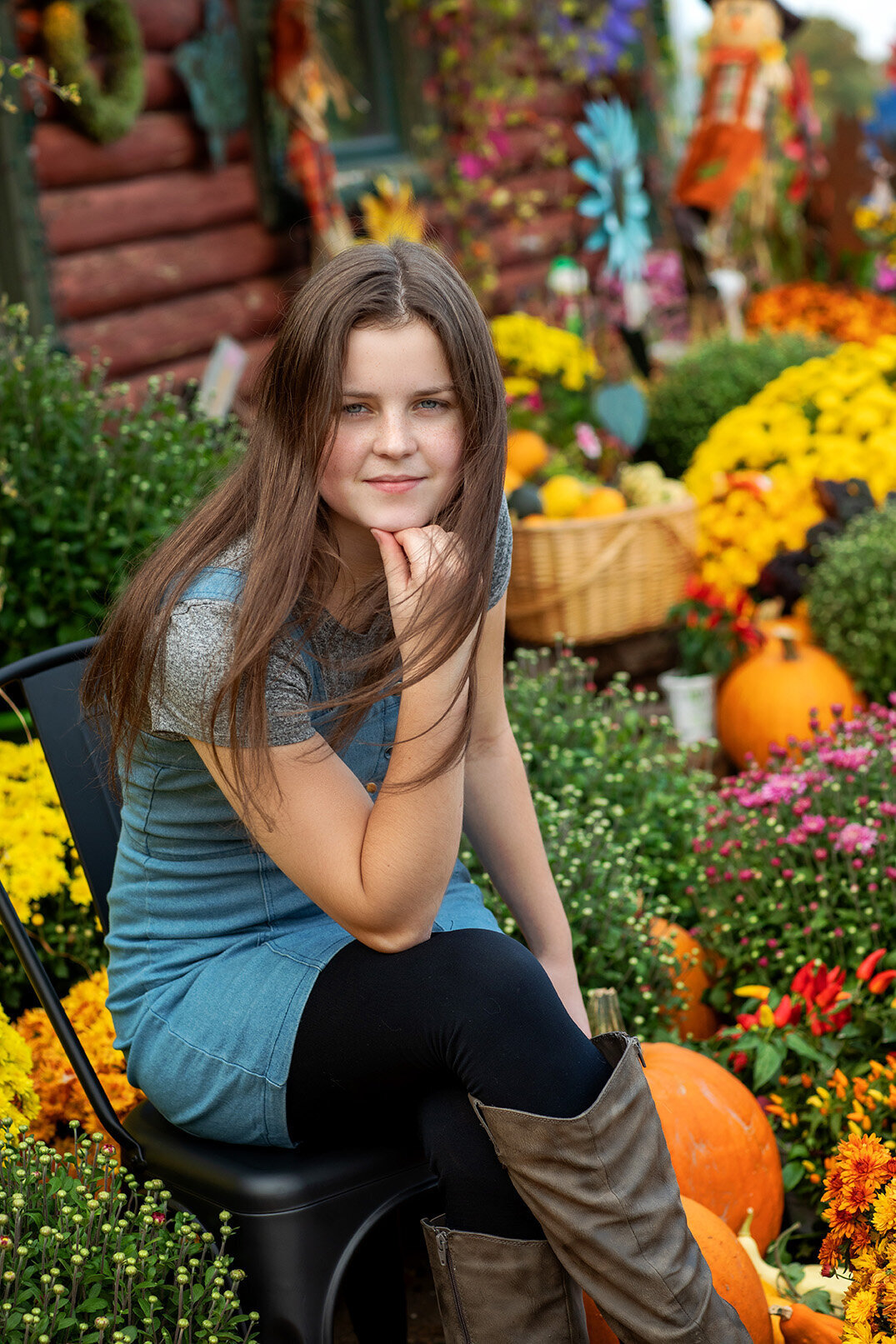 High school senior girl wearing jean romper sitting in a patch of fall flowers at Brittany's floral shop Walker, Minnesota.