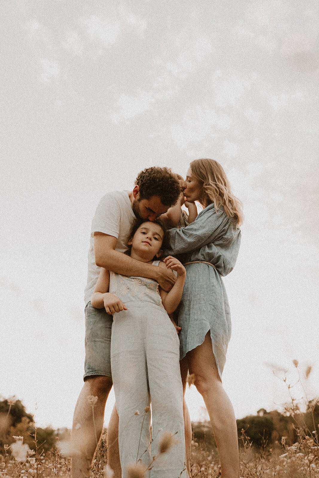 photo calin familial papa fait un bisous sur la tete de sa petite fille et la maman fait un bisous a son petit garcon dans un champ de fleurs alpes-maritimes