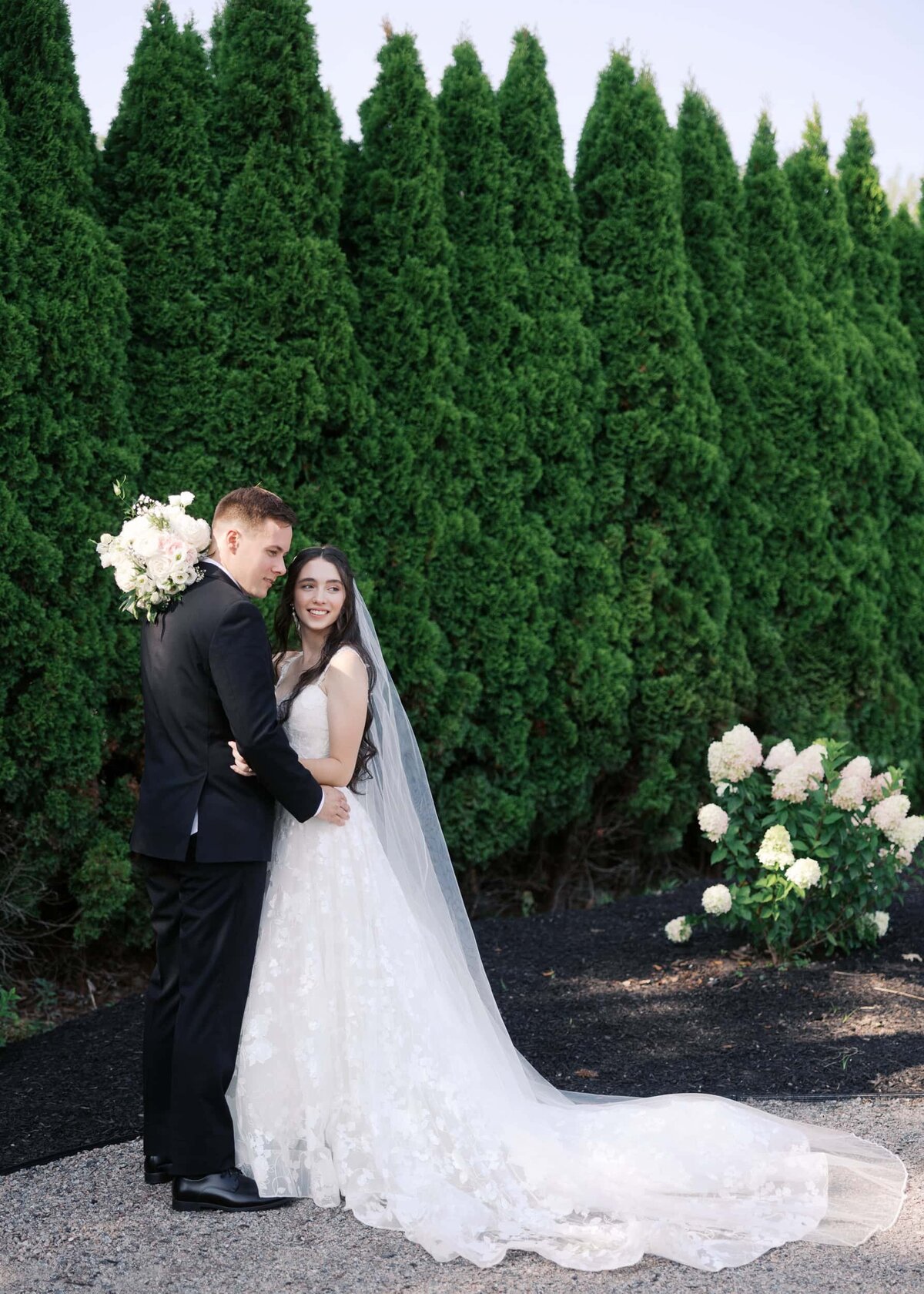 full body portrait of the bride and groom by the evergreens at Mohawk River Country Club