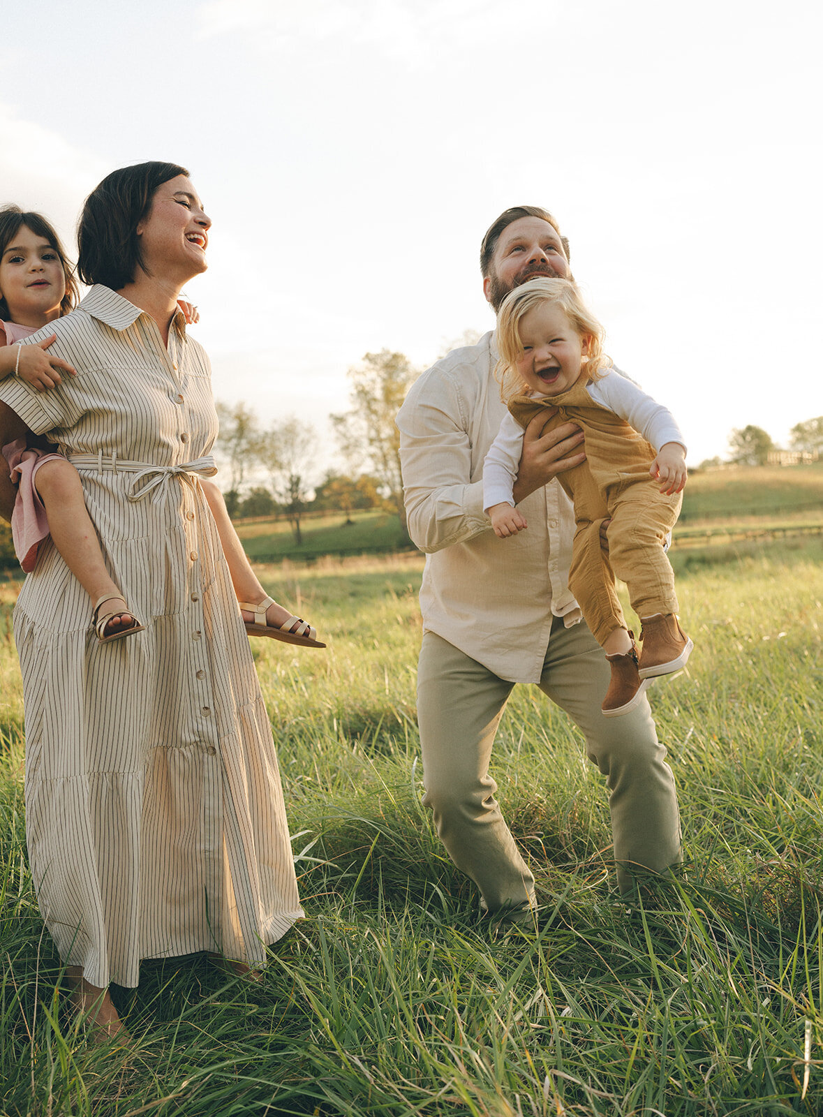 Father lifting one son in the air while mom holds another child piggyback-style during an energetic family session