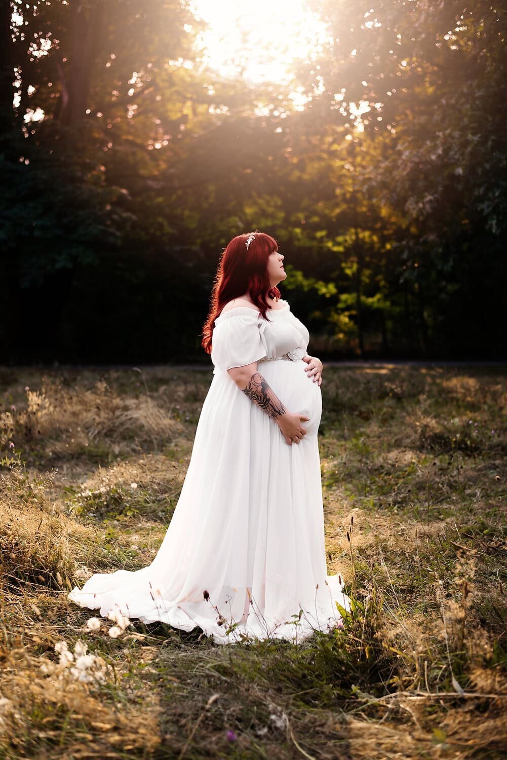 Expecting mom in a white gown posed in a field during sunset in Burnaby for a maternity photo shoot.