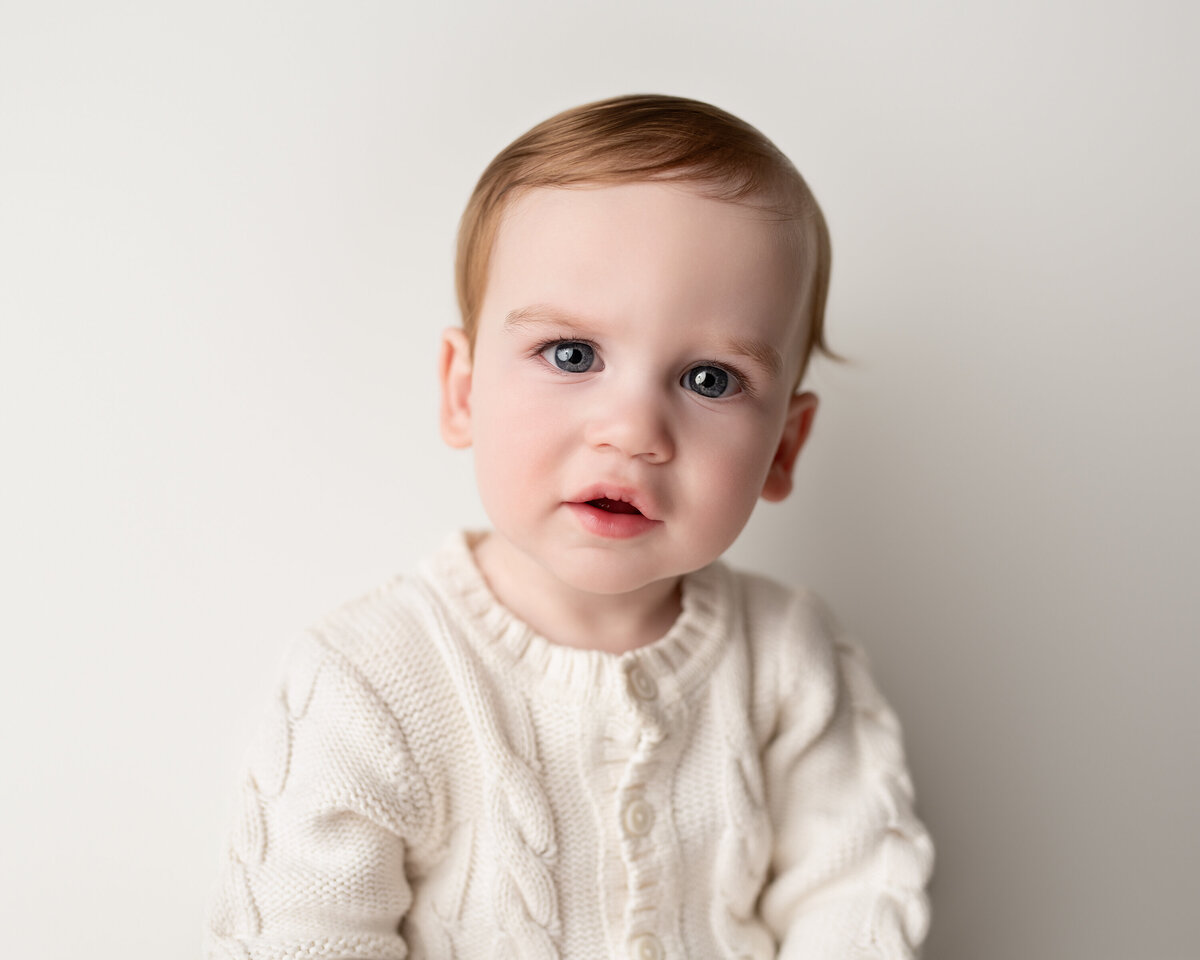 Clean, classic milestone studio portrait of a young boy in soft textures—perfect for timeless keepsakes.