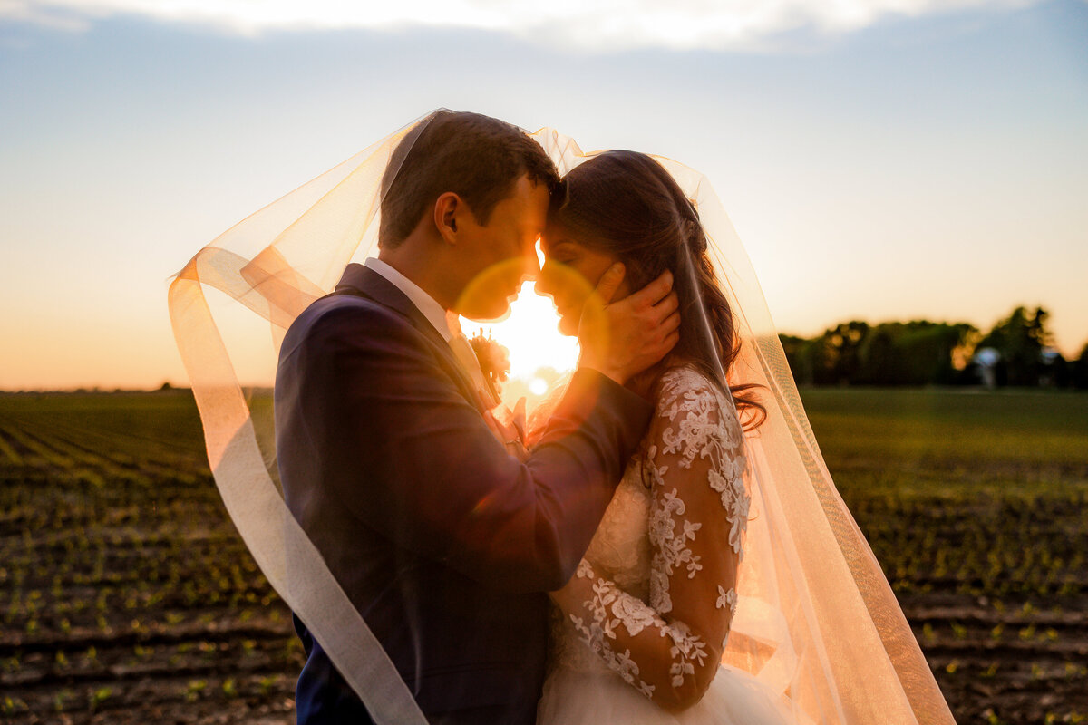 Bride and groom share an intimate moment under the veil at sunset.