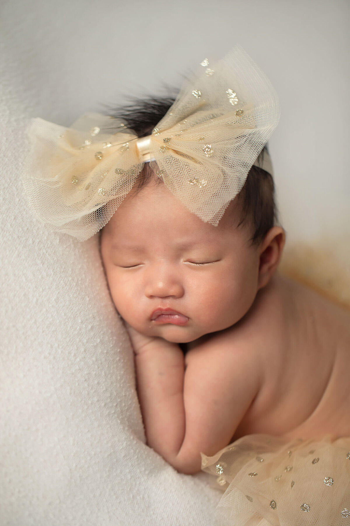 Sleeping newborn baby girl with a large cream colored bow headband.