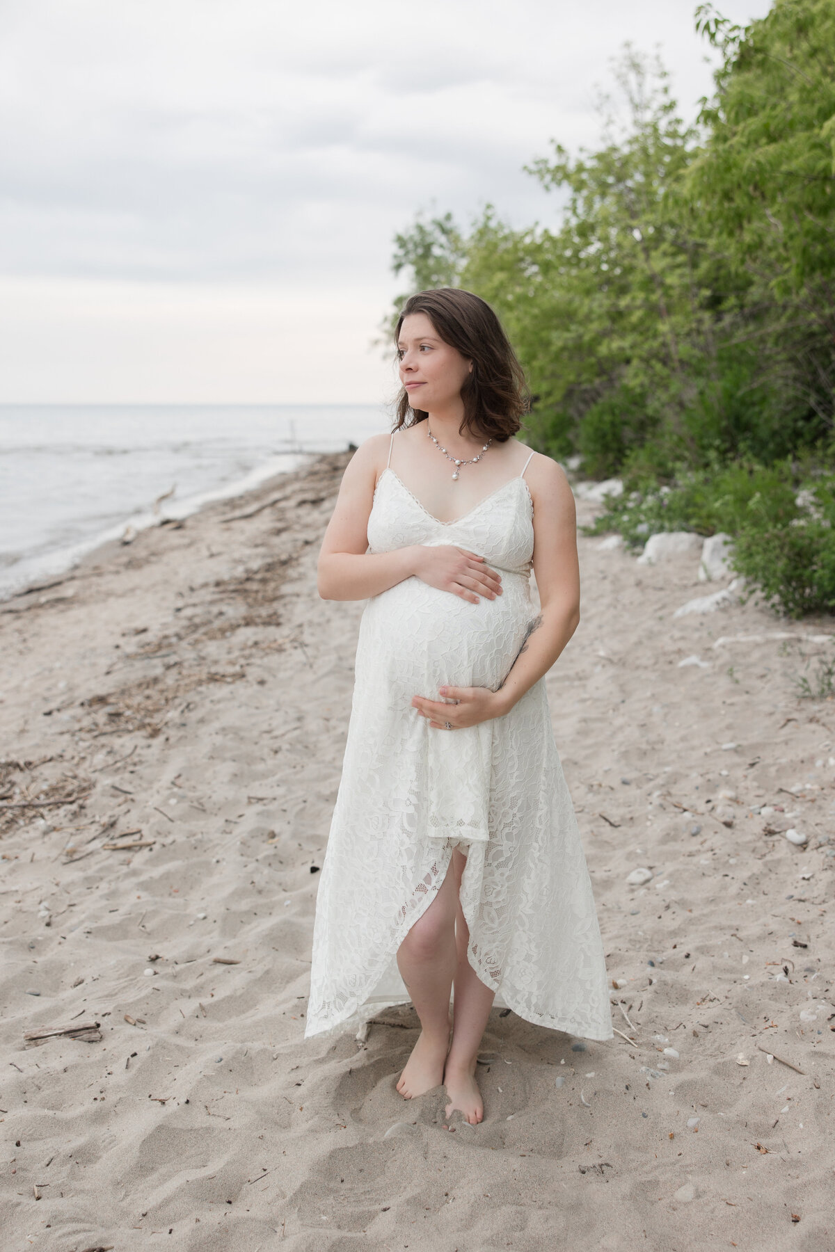 Expectant mother holding her baby bump and looking over the lake