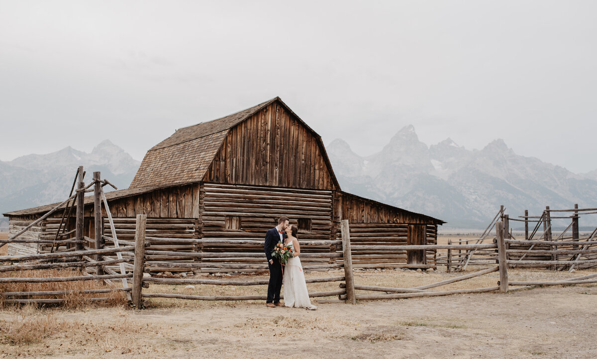 Photographers Jackson Hole capture bride and groom kissing in front of barn