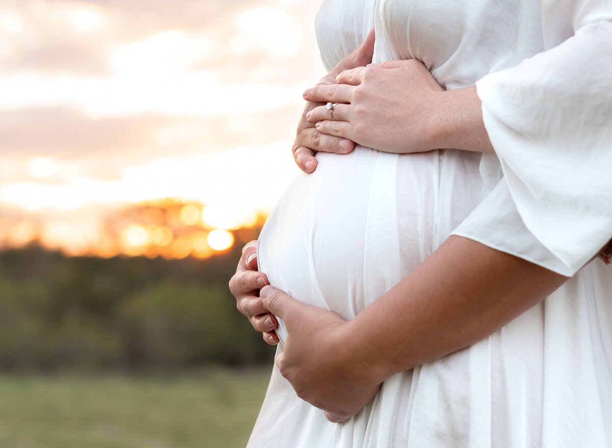Close-up of hands on baby bump during sunset maternity shoot near Austin, TX