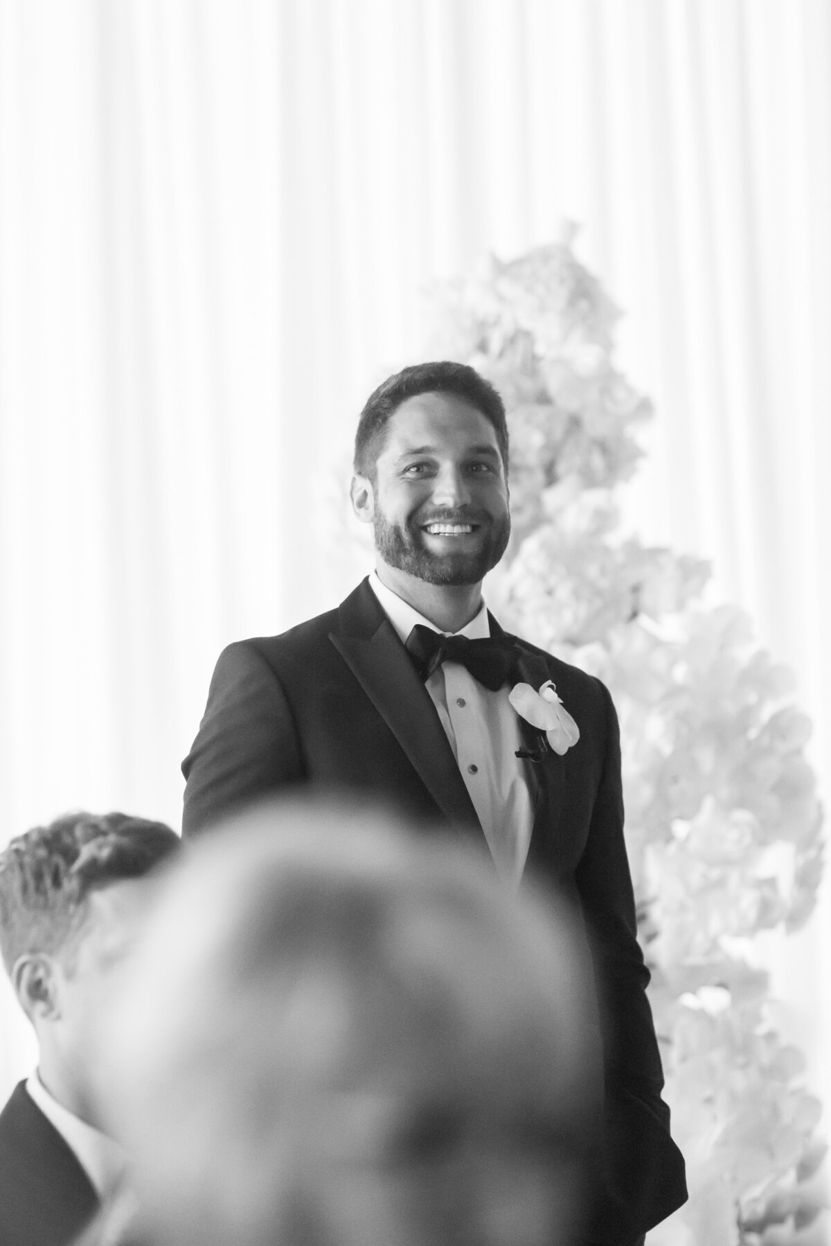 Groom smiles as he looks down the aisle at his bride approaching