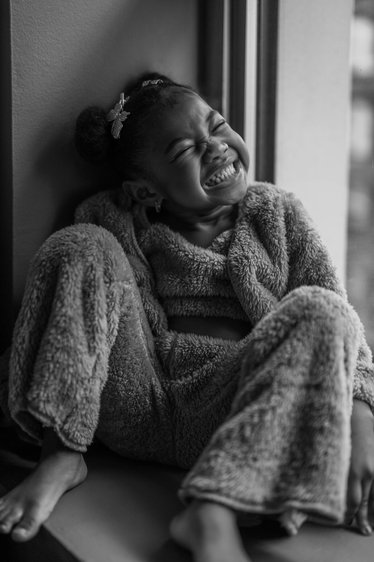 A joyful moment of a child laughing while sitting by the window, encapsulating the innocence and happiness of childhood during a NYC lifestyle family session.