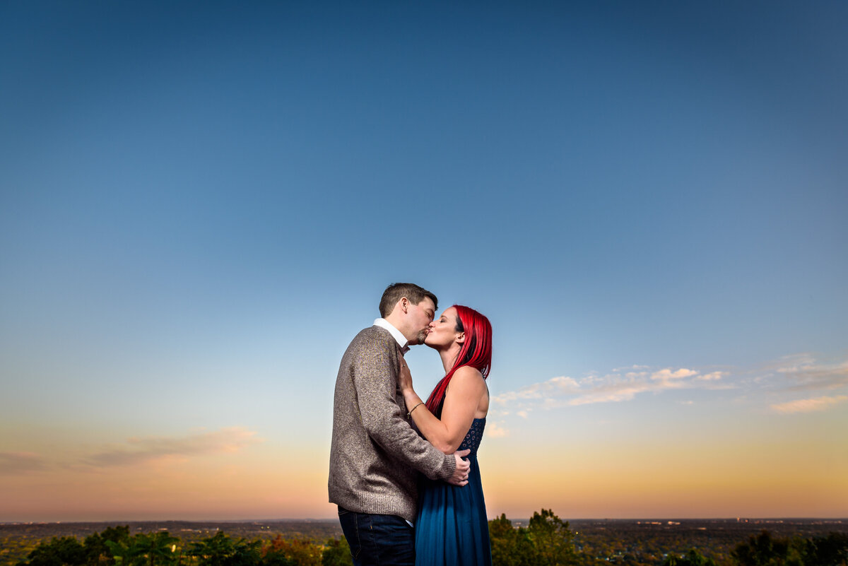 A couple kisses with the glowy sunset horizon as a backdrop