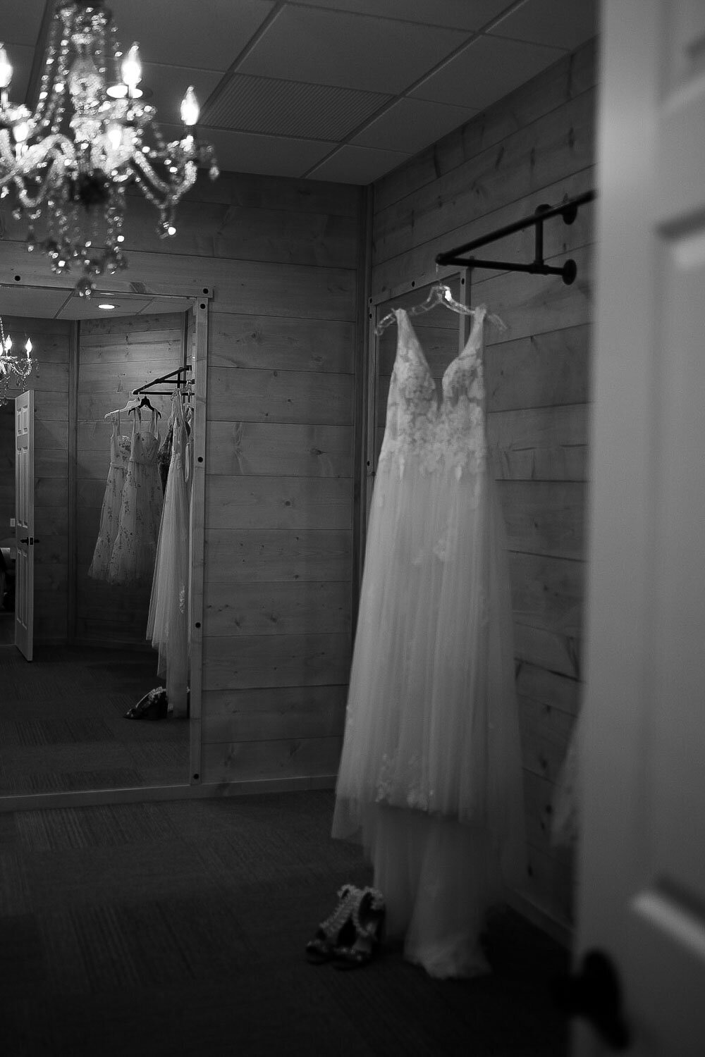 Black and white image of a wedding dress hanging in a mirror-lined room