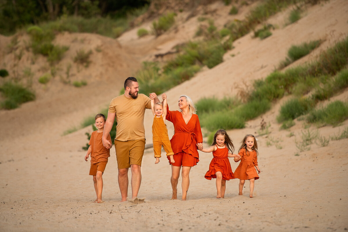 parents and children in matching outfits walking on the sand holding hands in Indiana dunes beach.