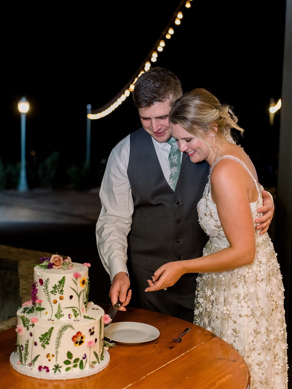 Bride and groom cut a wedding cake with pressed flowers on it.