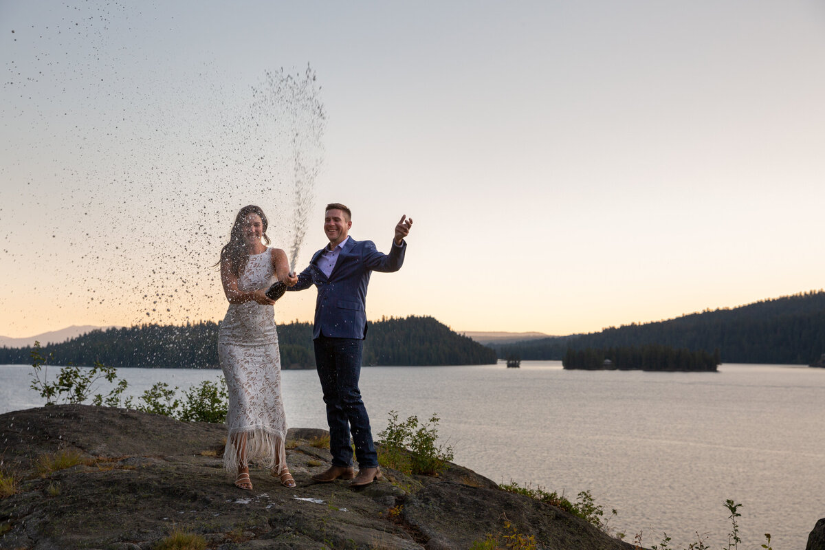 A bride pops champagne at her Idaho elopement photographer as her groom cheers her on.