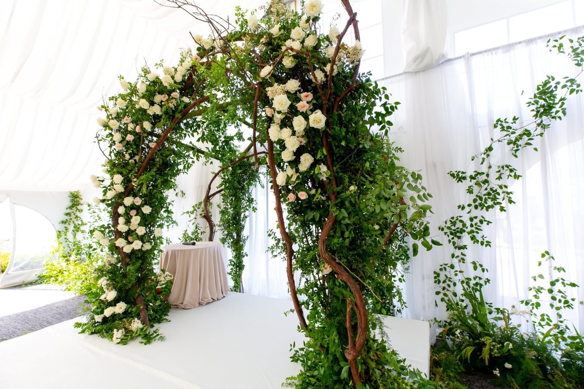Grand wedding arbor made of greenery, branches, and white flowers at Newcastle Golf course