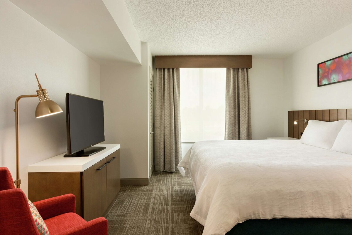 Modern queen hotel guest room with red lounge chair