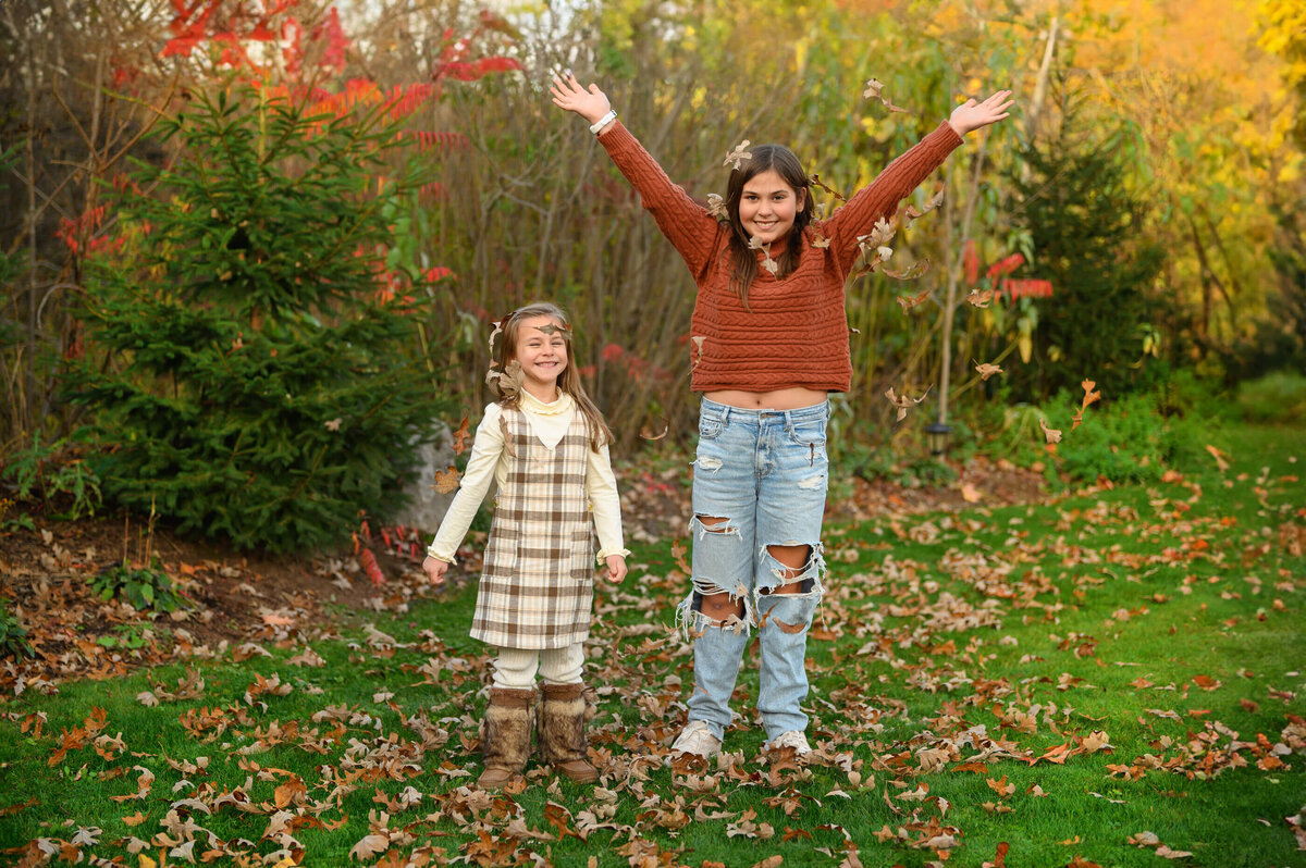 two sisters throwing leaves in their air for their family fall photos in Burlington, On