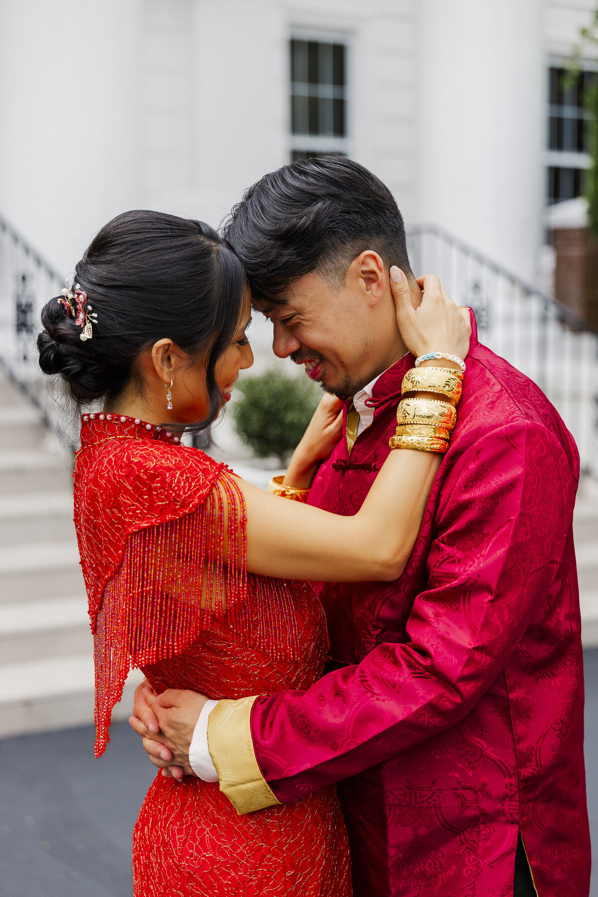 Couple in vibrant red wedding attire embracing with their foreheads touching