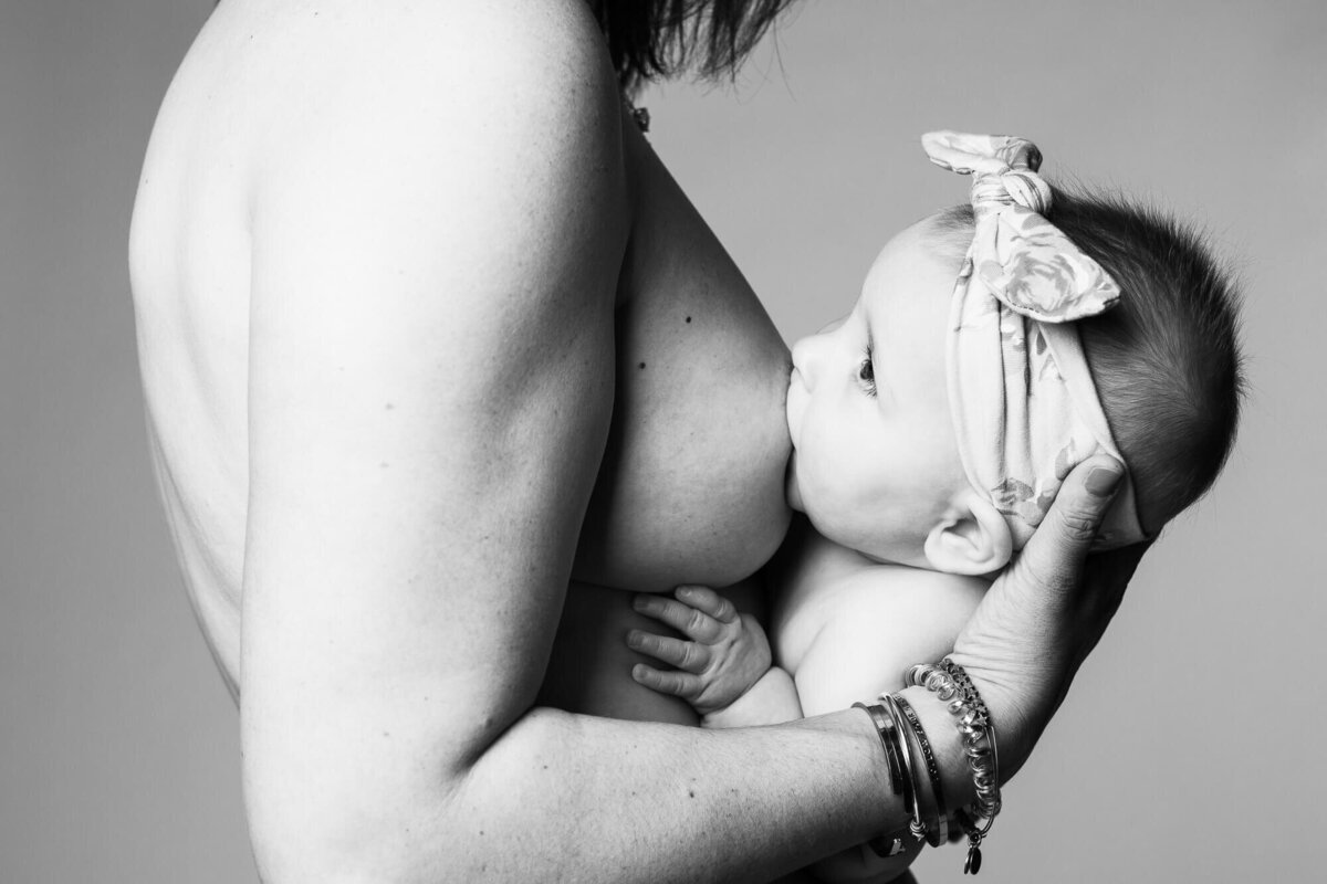 Black and white fine art studio portrait of mother breastfeeding her 6 month old baby.