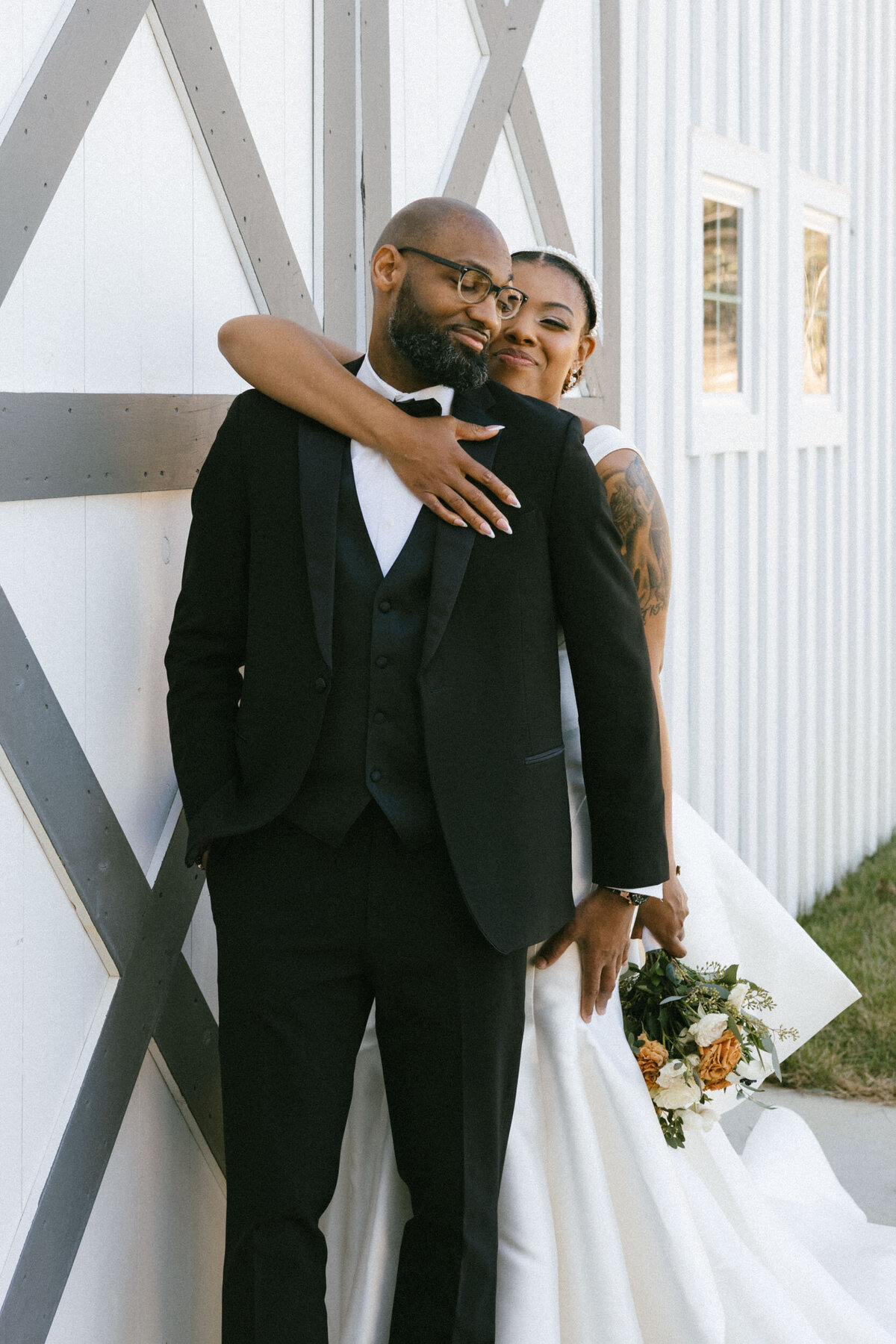 A couple embraces in front of a white barn at an outdoor elopement.