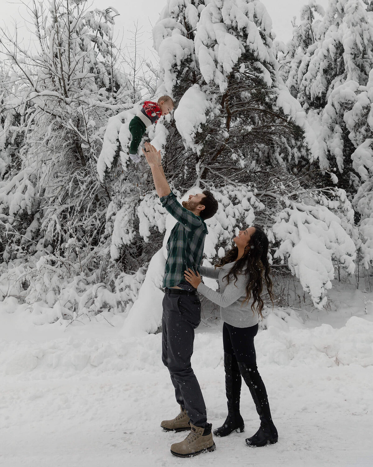 Dad throwing little boy up in the air while mom is standing behind dad watching. Beautiful snowy day.