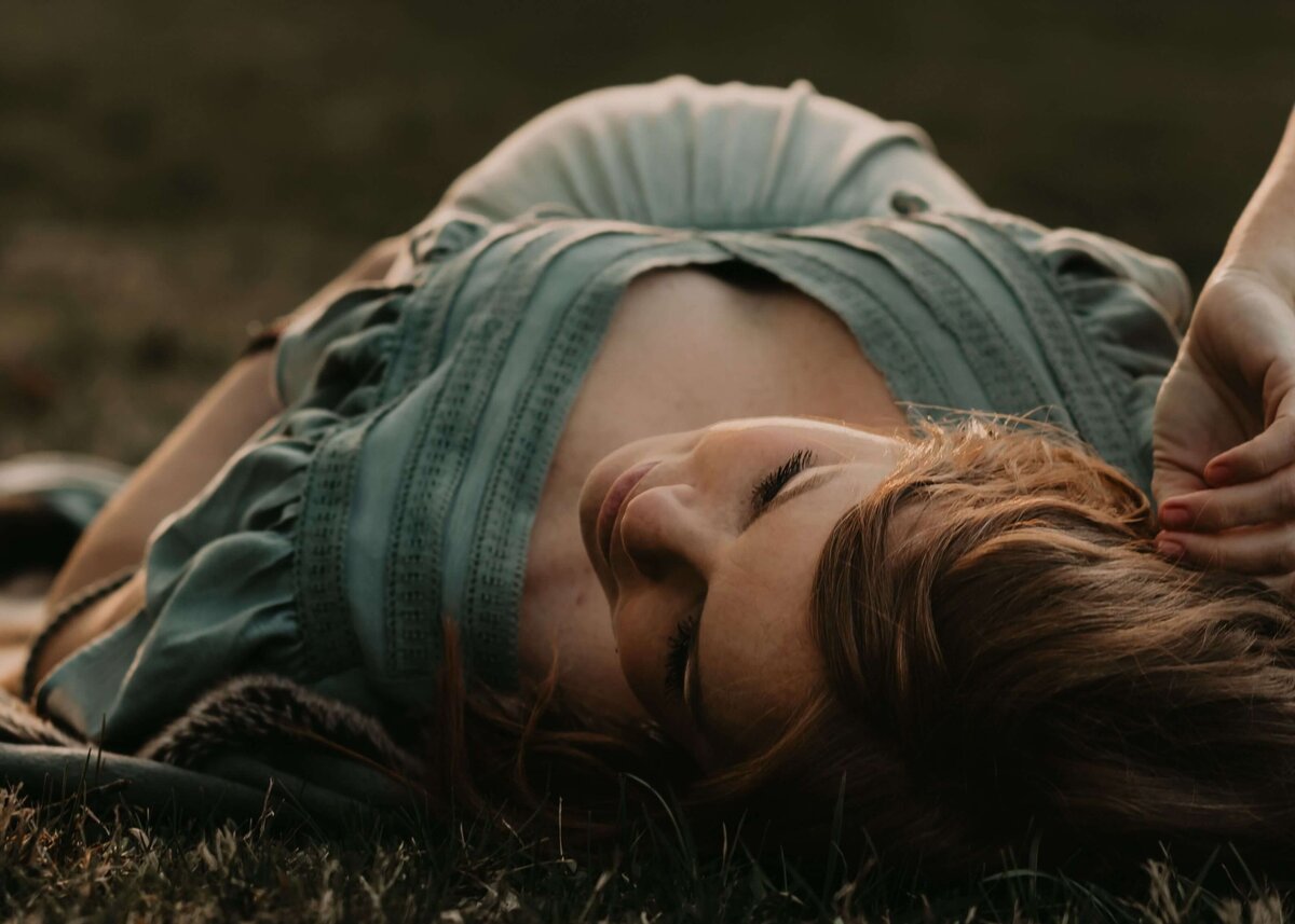 A woman is laying in the grass with her hair pulled back, captured by a Pittsburgh maternity photographer.