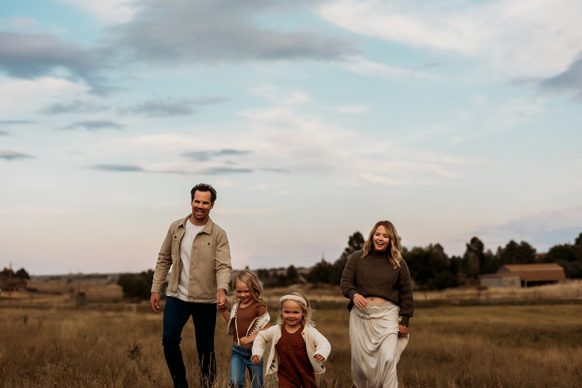 two young sisters running in a tall grassy field while mom and dad walk slowly behind them.