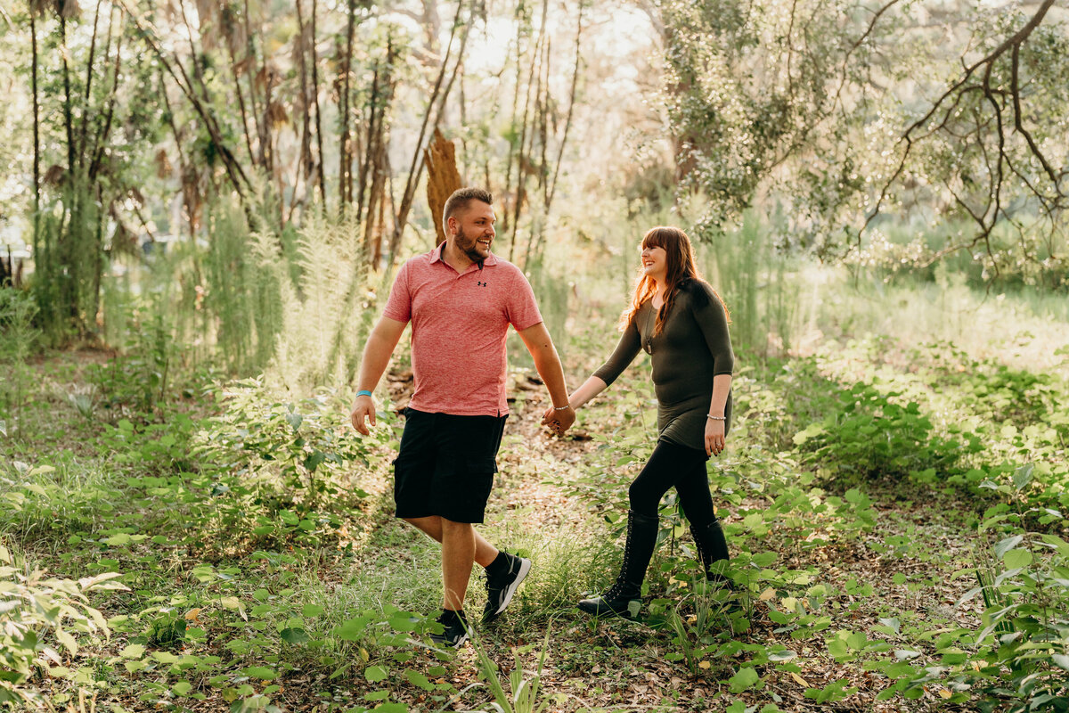 couple walking through the woods during engagement session holding hands and smiling at eachother